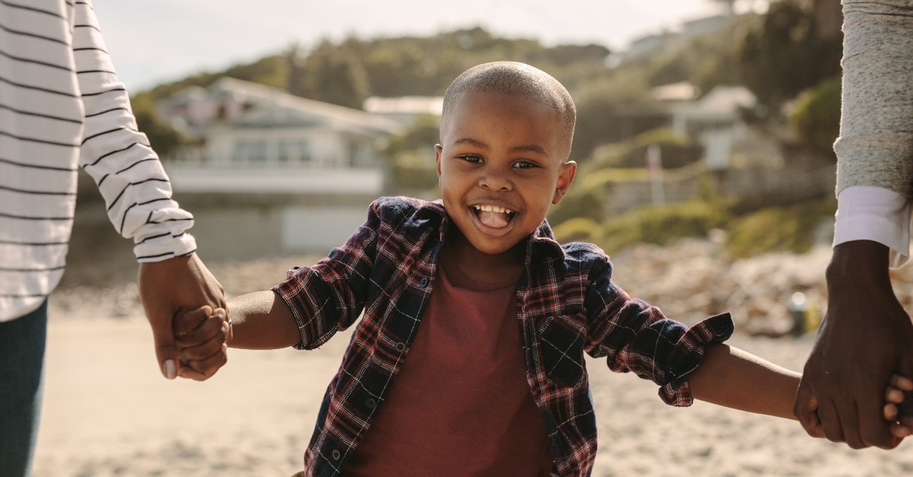 young boy looking happy holding his parents hands walking down beach