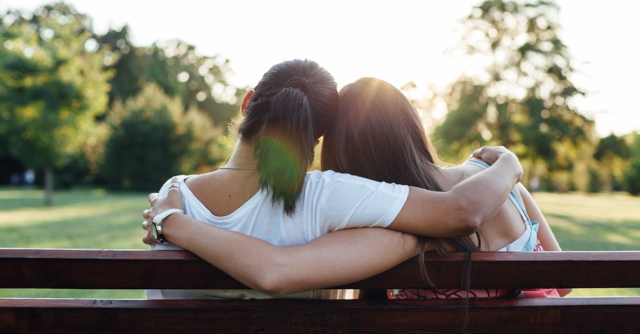 two women hugging sitting on bench