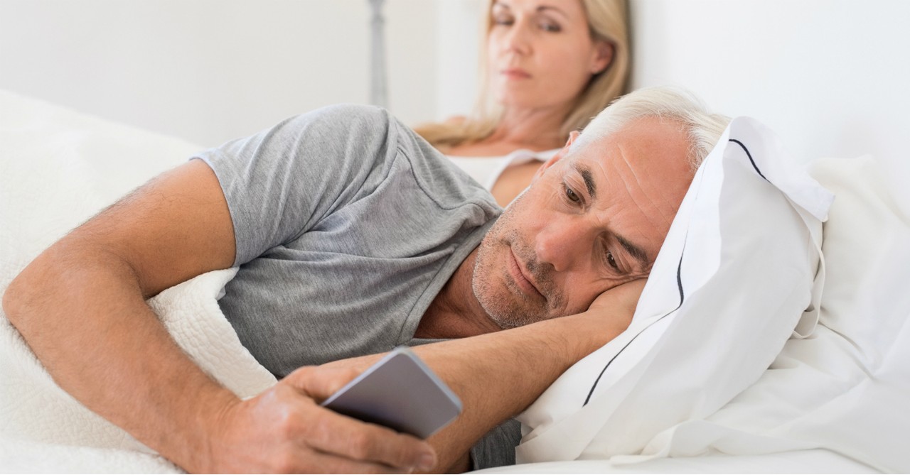 senior husband in bed with wife ignoring cell phone smartphone